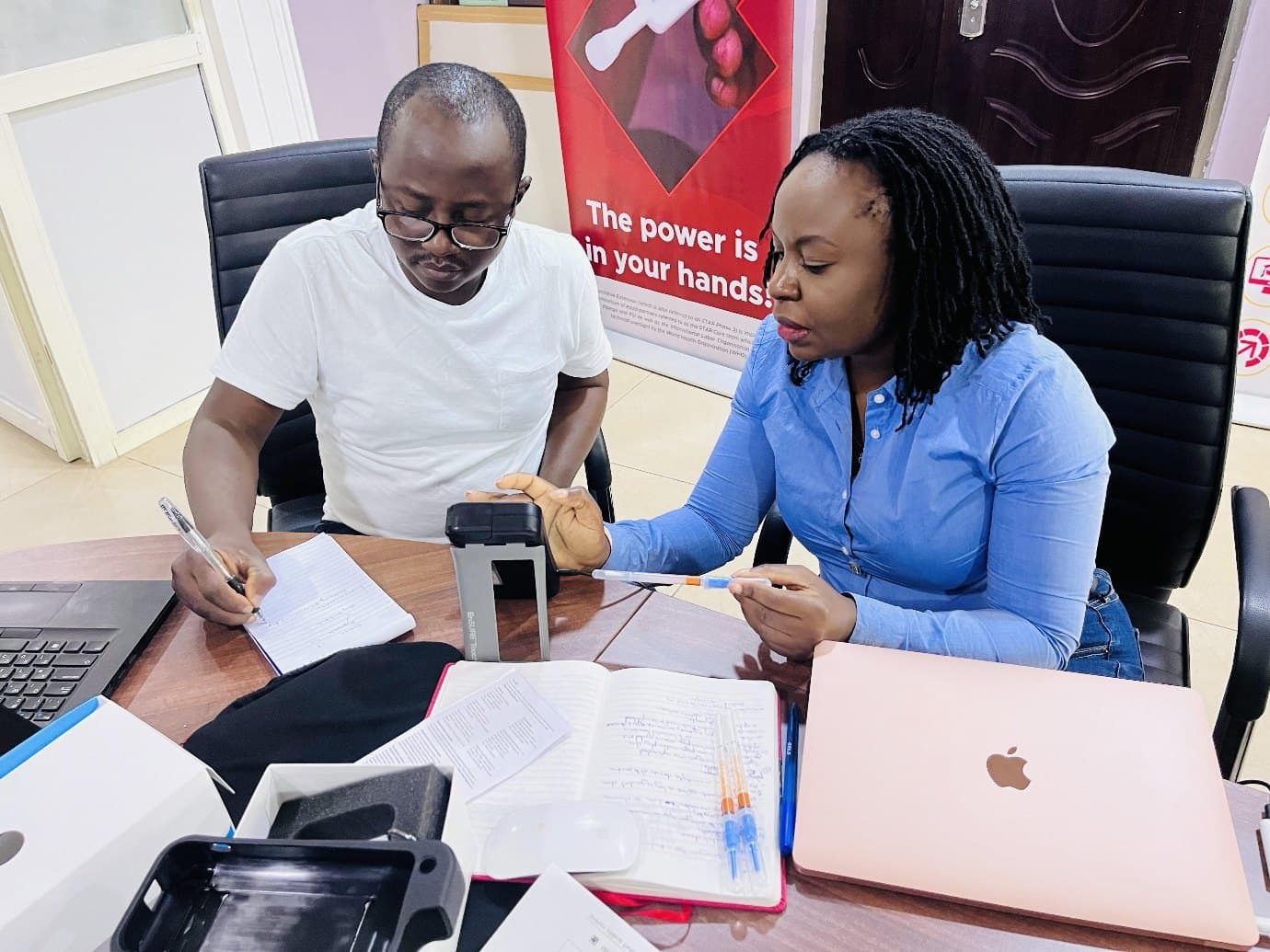 Two people seated at a desk working with an ATP monitoring device and printed records.