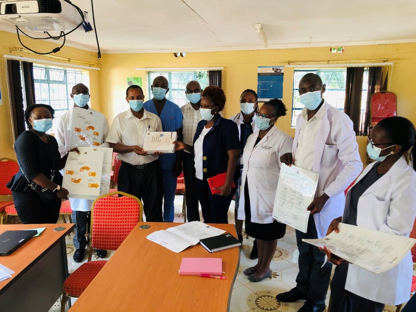 Health care workers in masks holding printed IPC job aids and guideline documents.