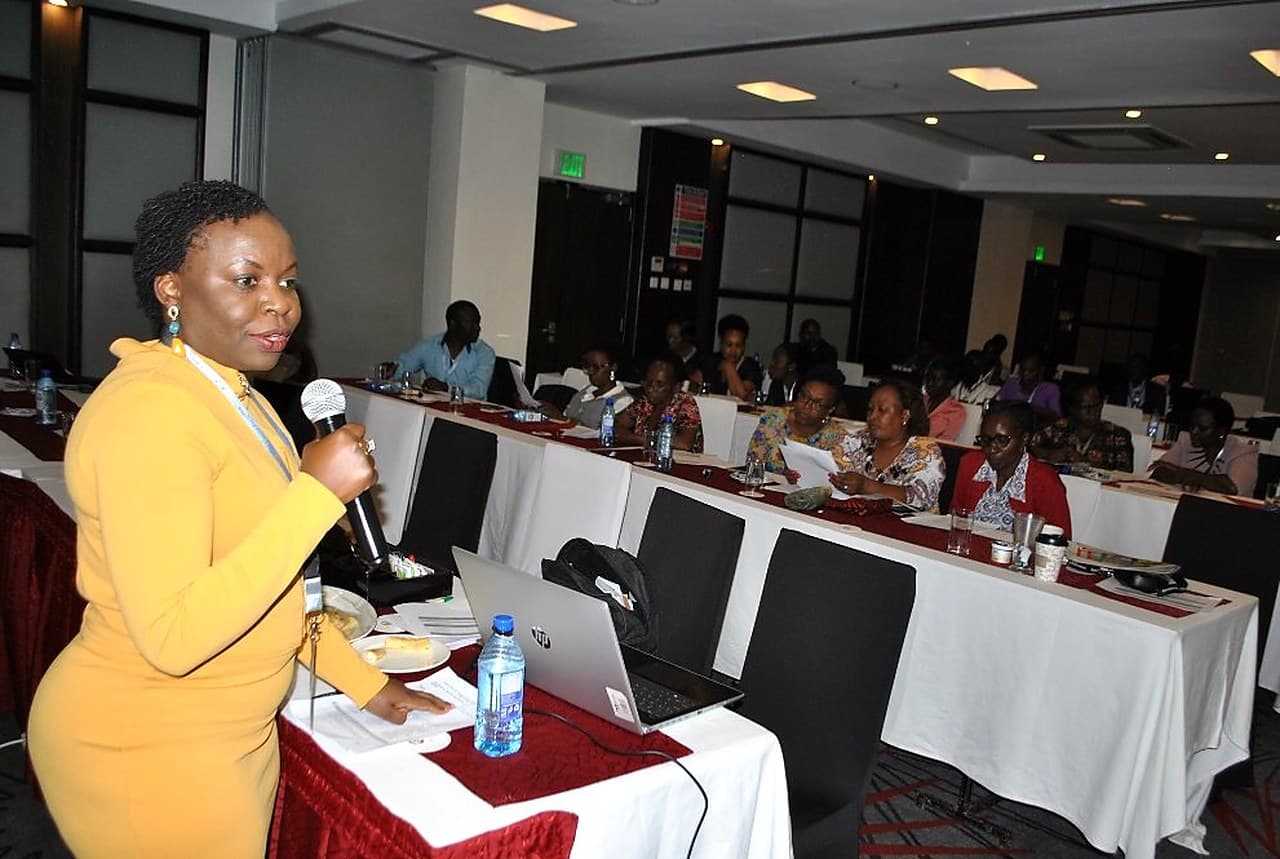 Doris Bota facilitating a conference session with a microphone, delegates seated at tables.