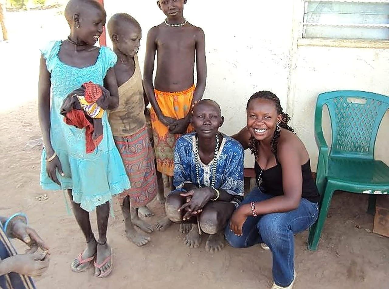 Doris Bota crouching beside a group of children outside a community health building.